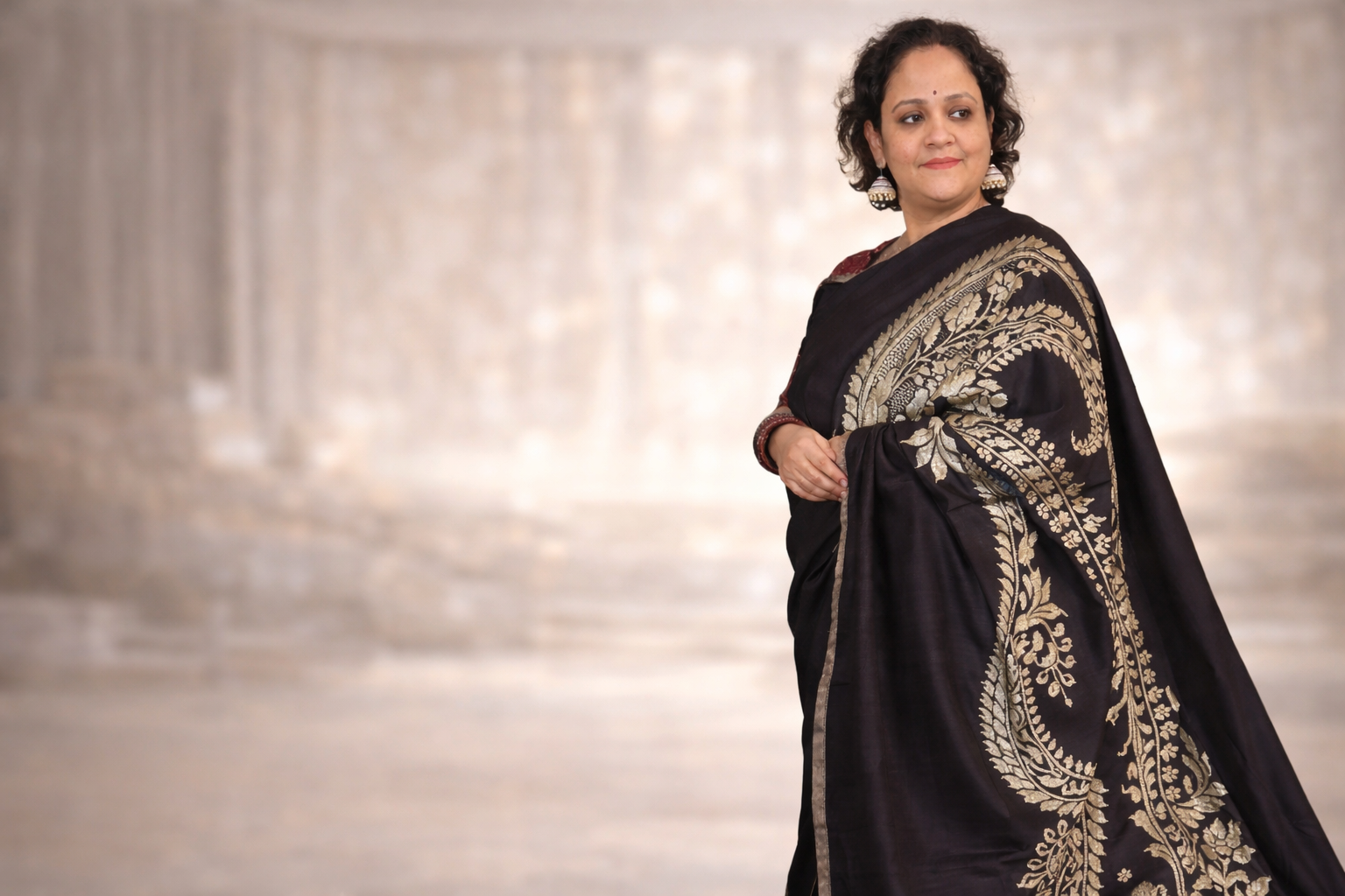Woman wearing a black saree with gold embroidery against a blurred background